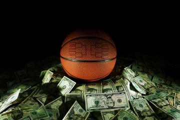 A basketball with a bracket engraved in it sits on a pile of U.S. currency.